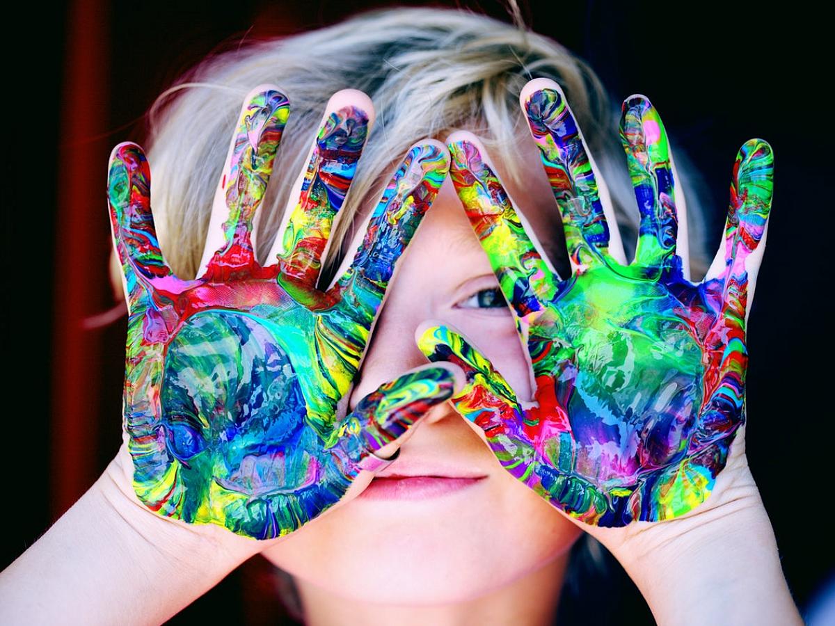 Child with paint on hands holding them in front of his face